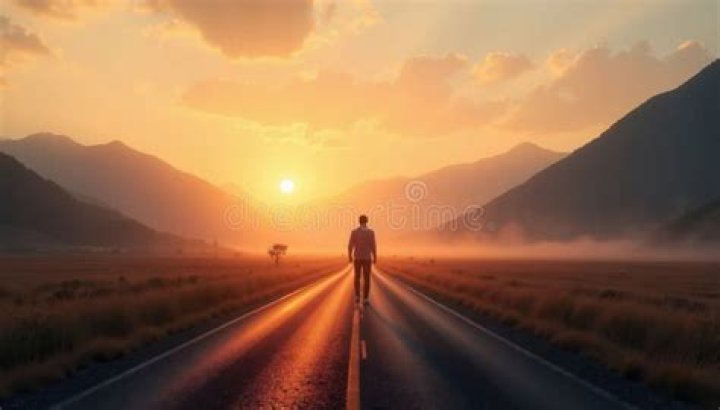 person walking on road toward colorful mountains